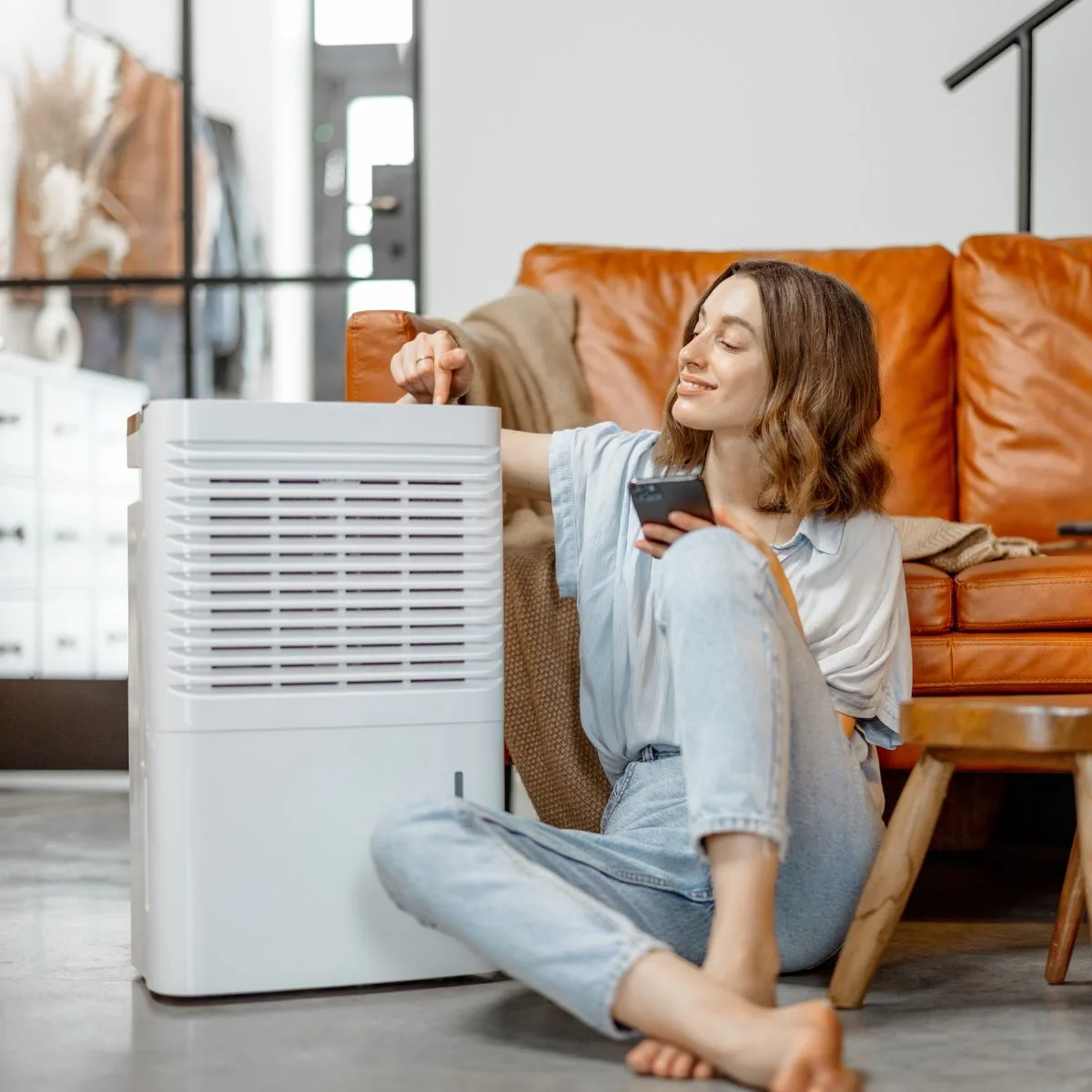 A woman sitting in a living room on the floor next to a dehumidifier.