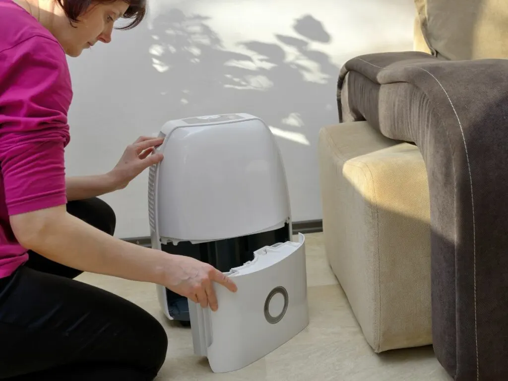 A woman opening and preparing to clean a dehumidifier on the floor.