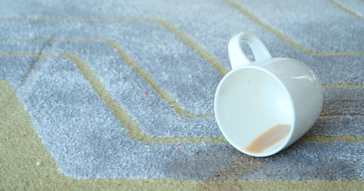 A coffee cup is accidentally spilled, resulting in a stain on a rug.