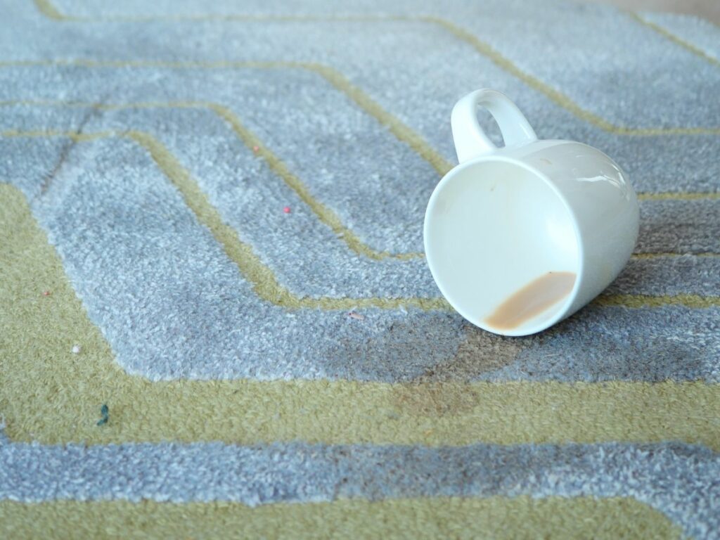 A coffee cup spilling coffee on a grey and yellow rug.