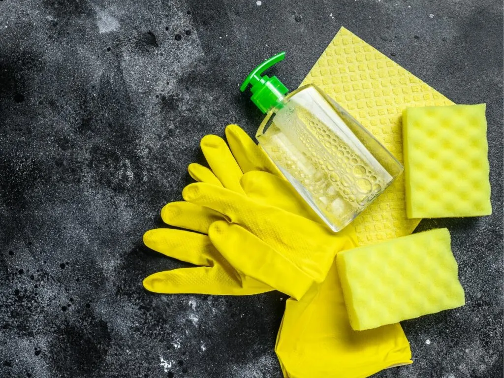 Yellow cleaning gloves and a bottle of cleaning liquid on a dark background.