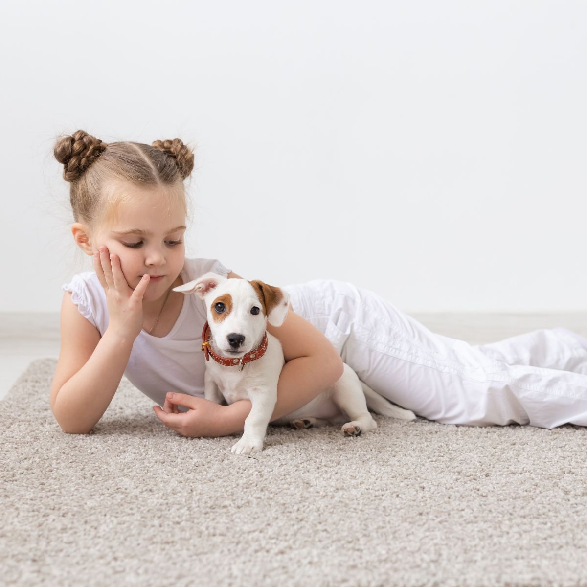 A little girl laying on the carpet with a young puppy.