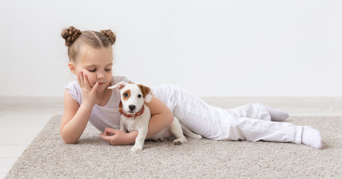 A little girl laying on the carpet with a young puppy.