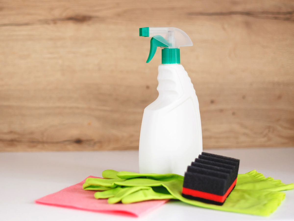 A bottle of cleaning spray and a pair of gloves on a wooden table, showing how to clean stains out of carpet.
