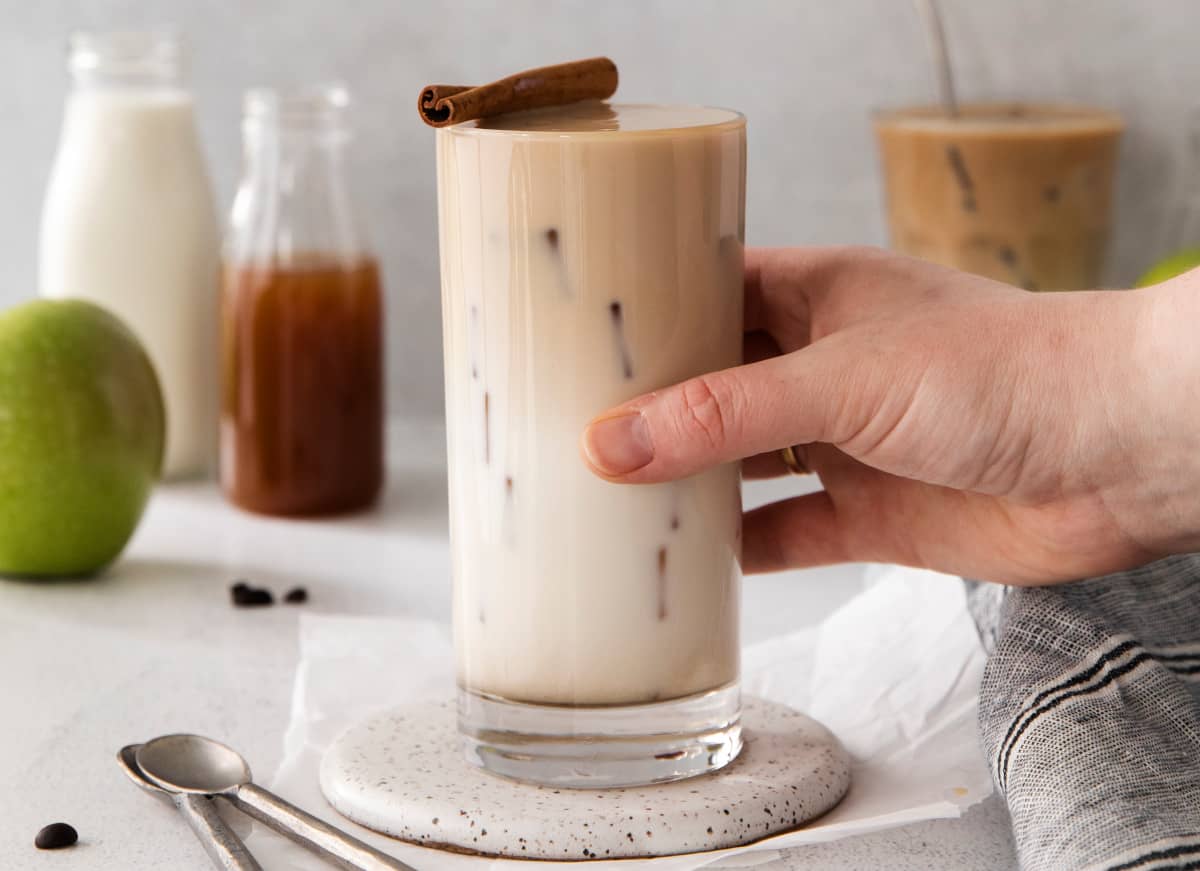 A person holding a glass of iced coffee with a cinnamon stick.