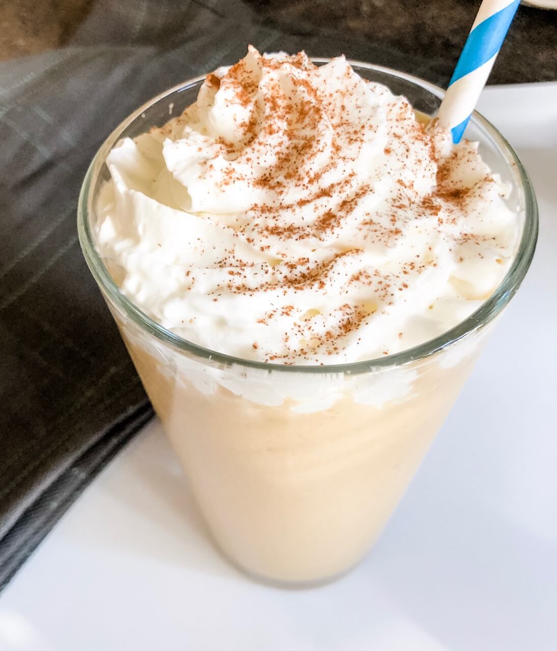 A glass of coffee with whipped cream and a straw.