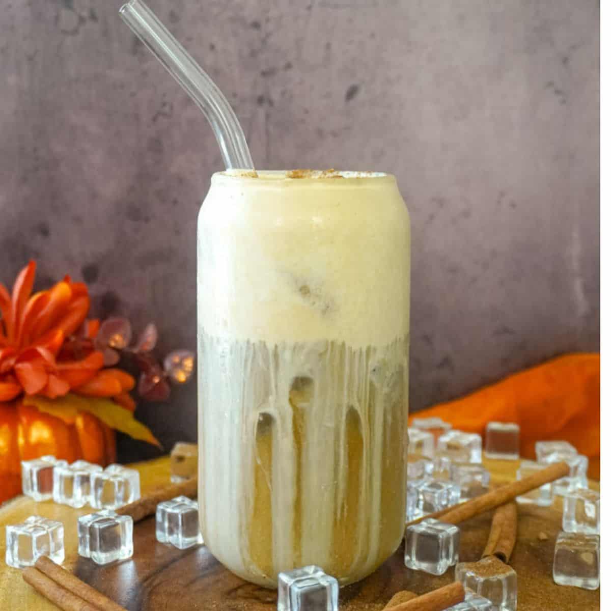 A pumpkin spice latte in a glass with ice cubes.
