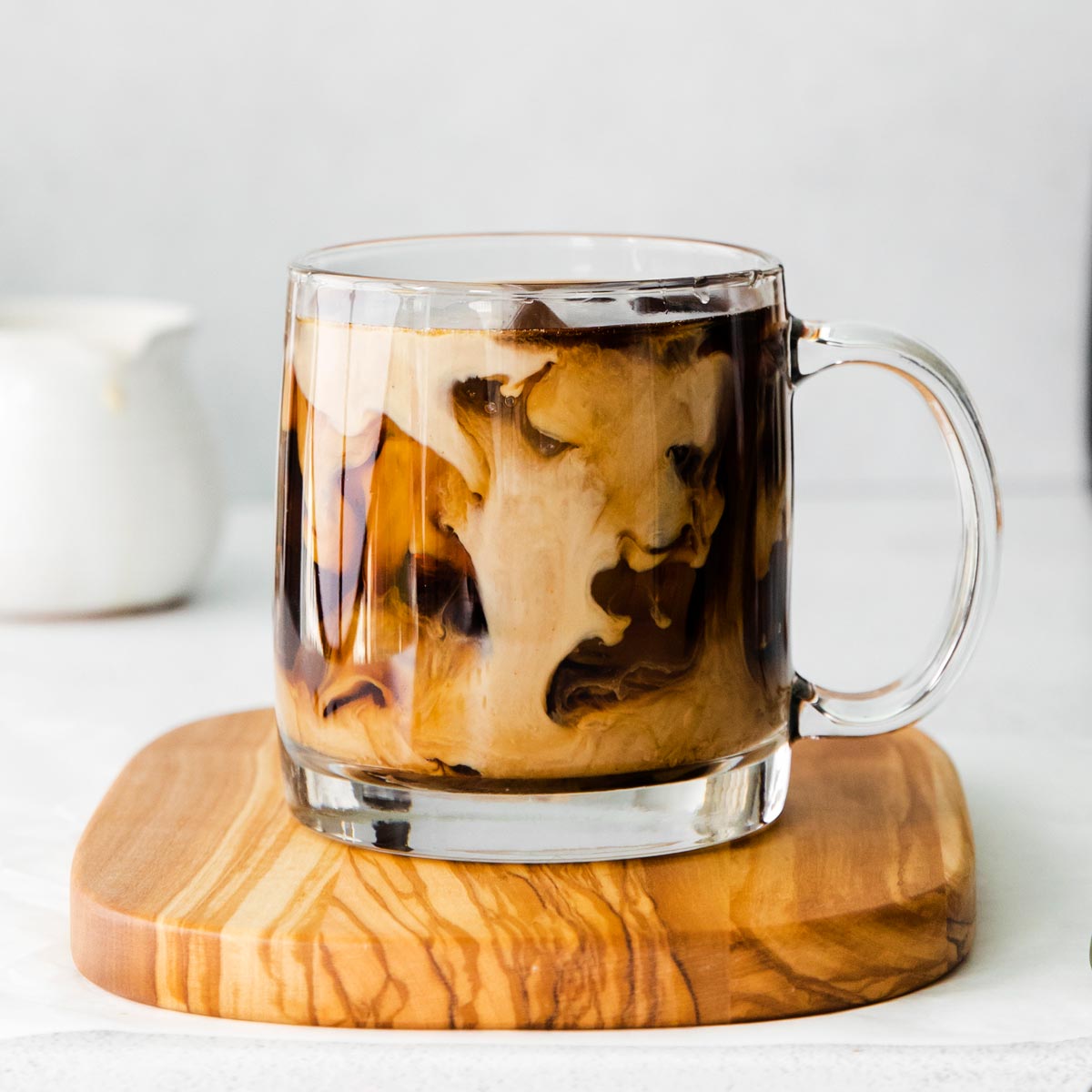 A cup of iced coffee on a wooden cutting board.