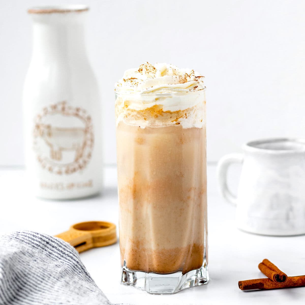 A glass of coffee with whipped cream and cinnamon sticks.