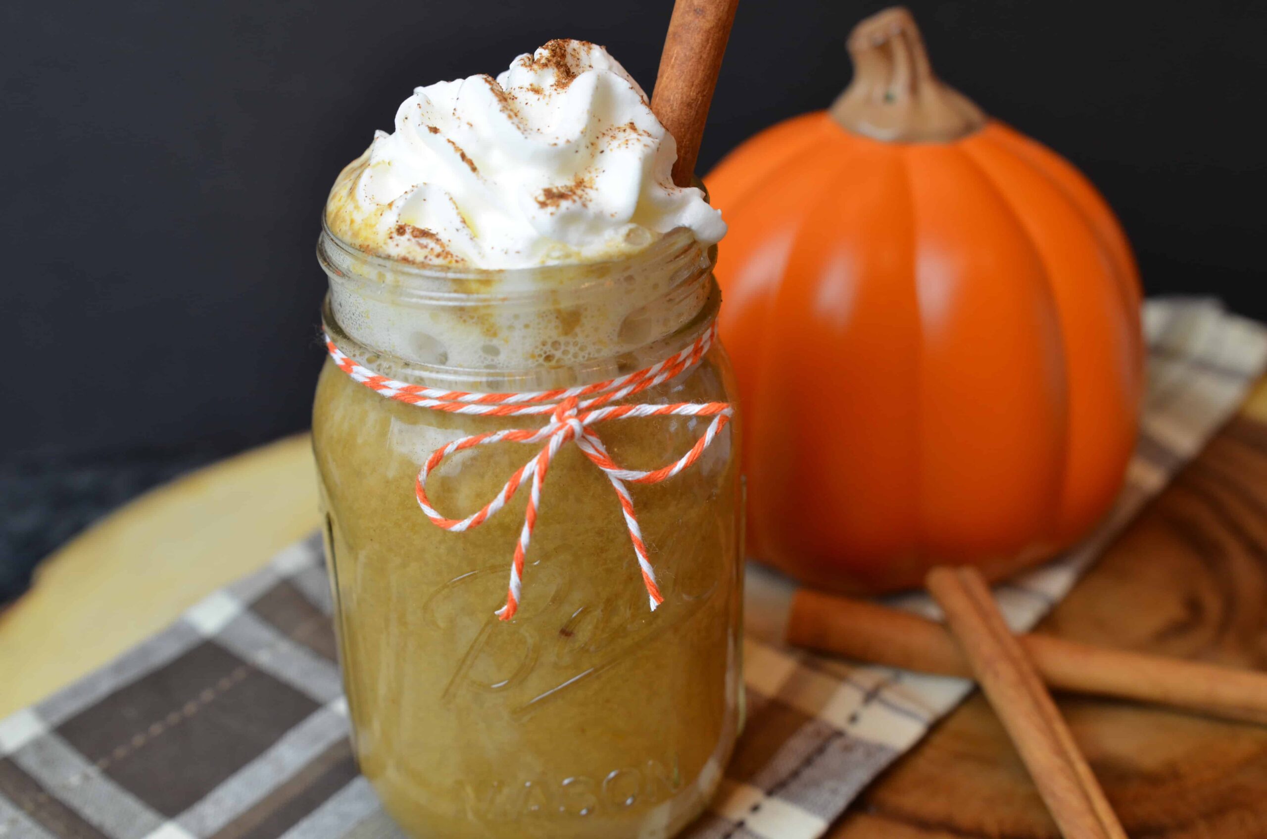 A pumpkin spice latte in a mason jar next to a pumpkin and cinnamon sticks.