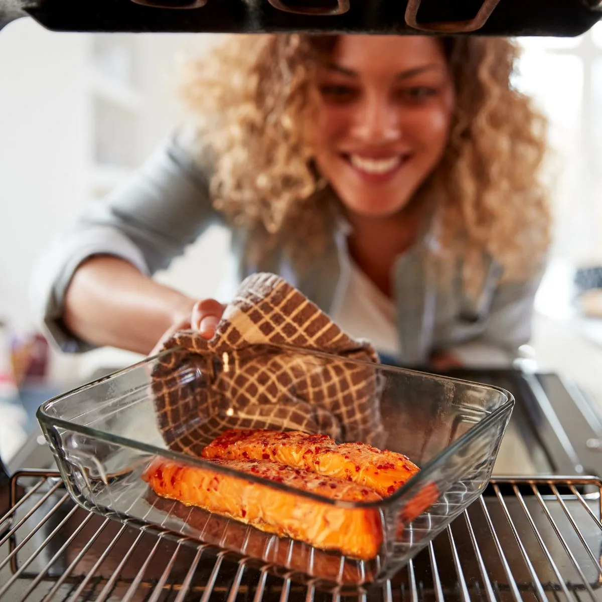 A woman checking a seafood dish in an oven.