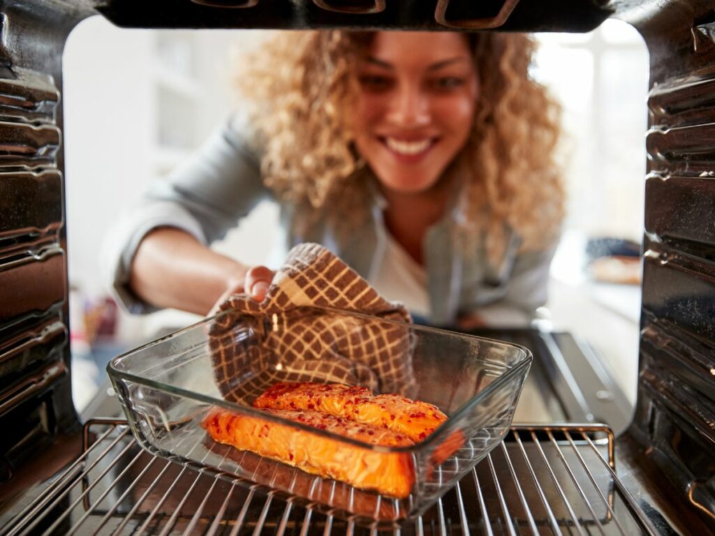 A woman is preparing salmon in the oven.