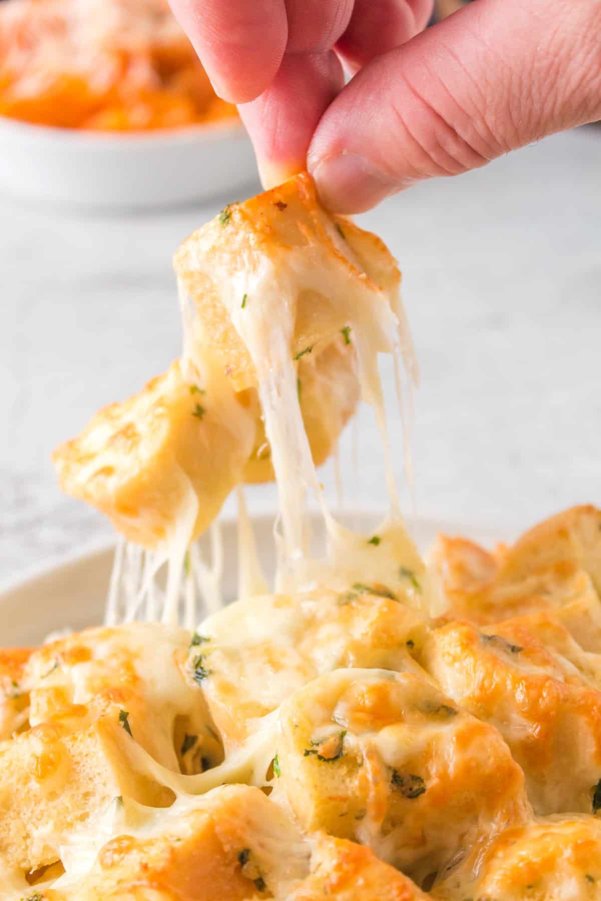 A person lifting up cheesy bread from a plate.