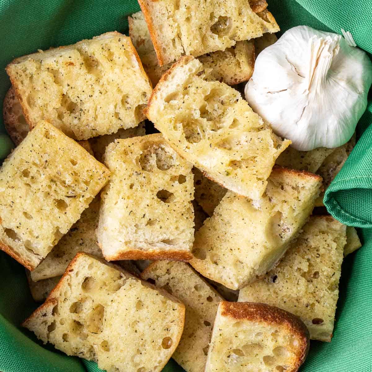 Garlic bread in a green bowl with a head of garlic.