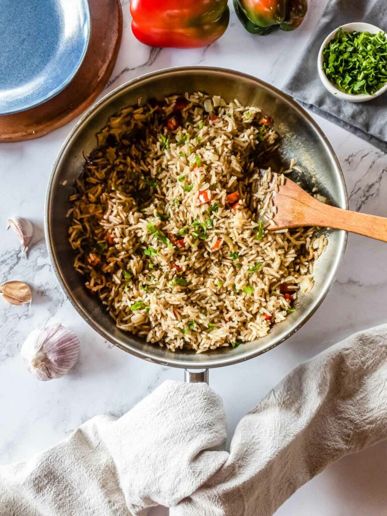 A pan full of easy rice pilaf and vegetables with a wooden spatula.