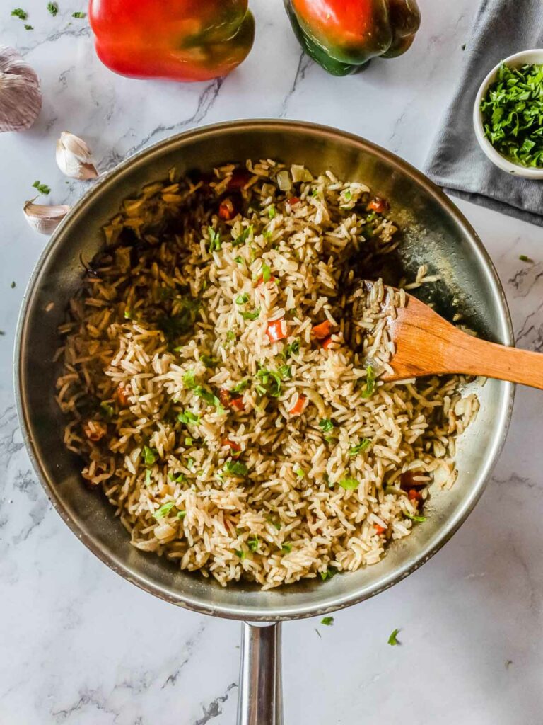 A pan with rice and garnish next to a wooden spatula.