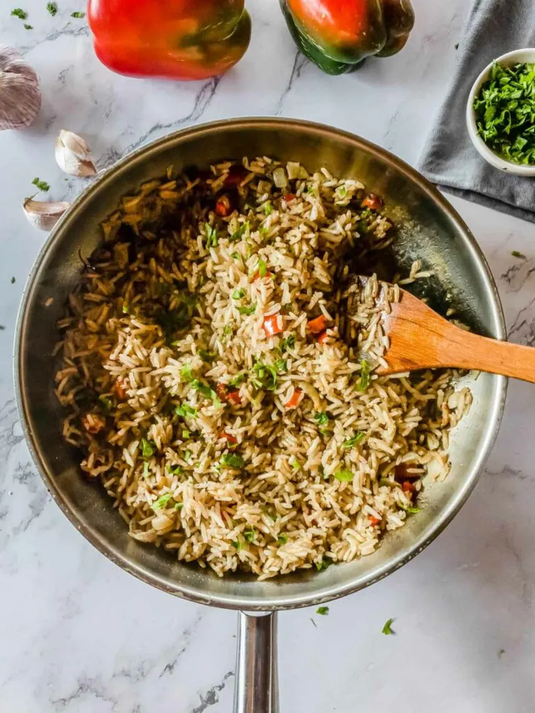 A pan with rice and peppers next to a wooden spatula.