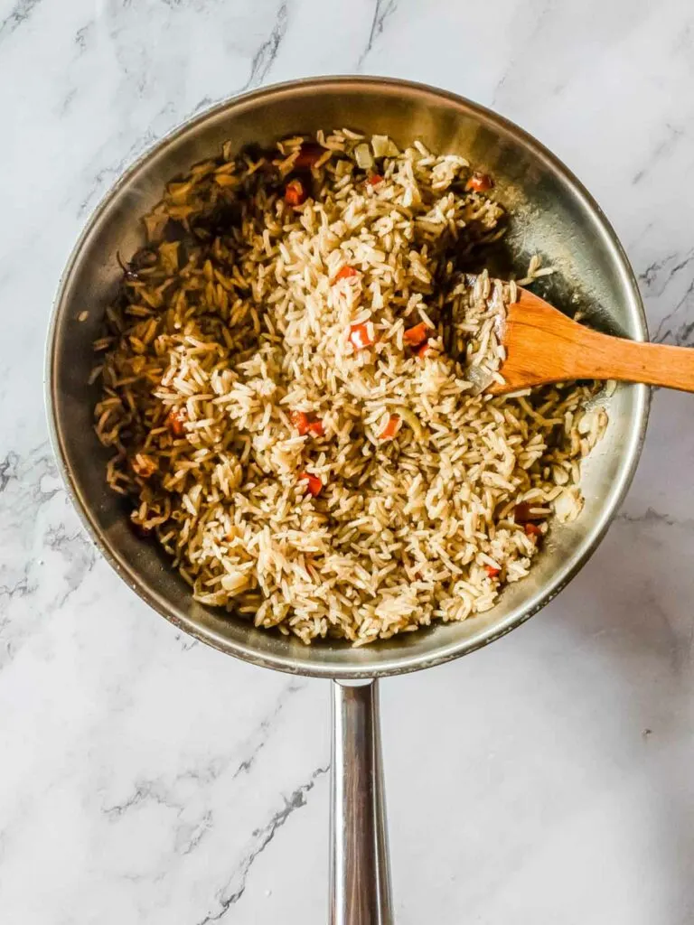 Browned cooked rice in a pan with a wooden spatula.