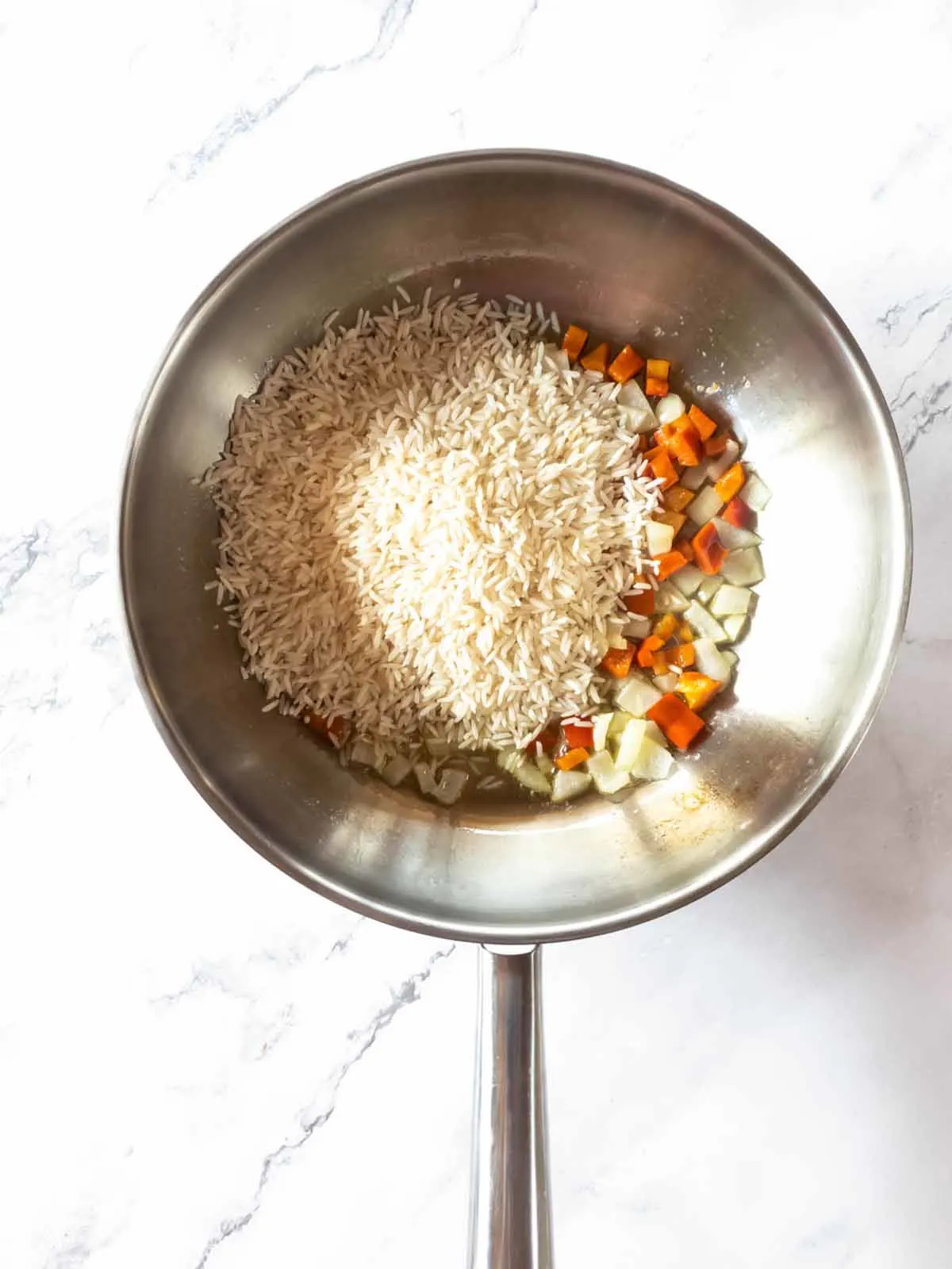 A skillet filled with uncooked rice and vegetables.