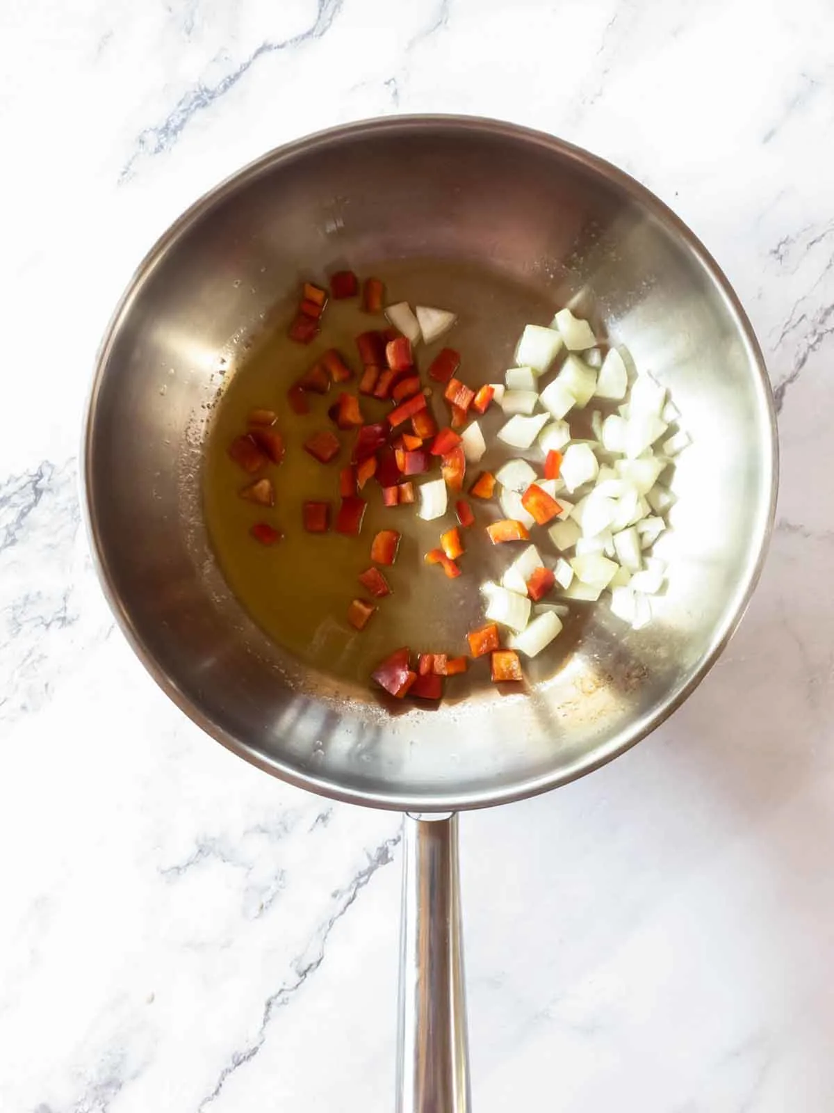 A frying pan with chopped white onions and red peppers in it.