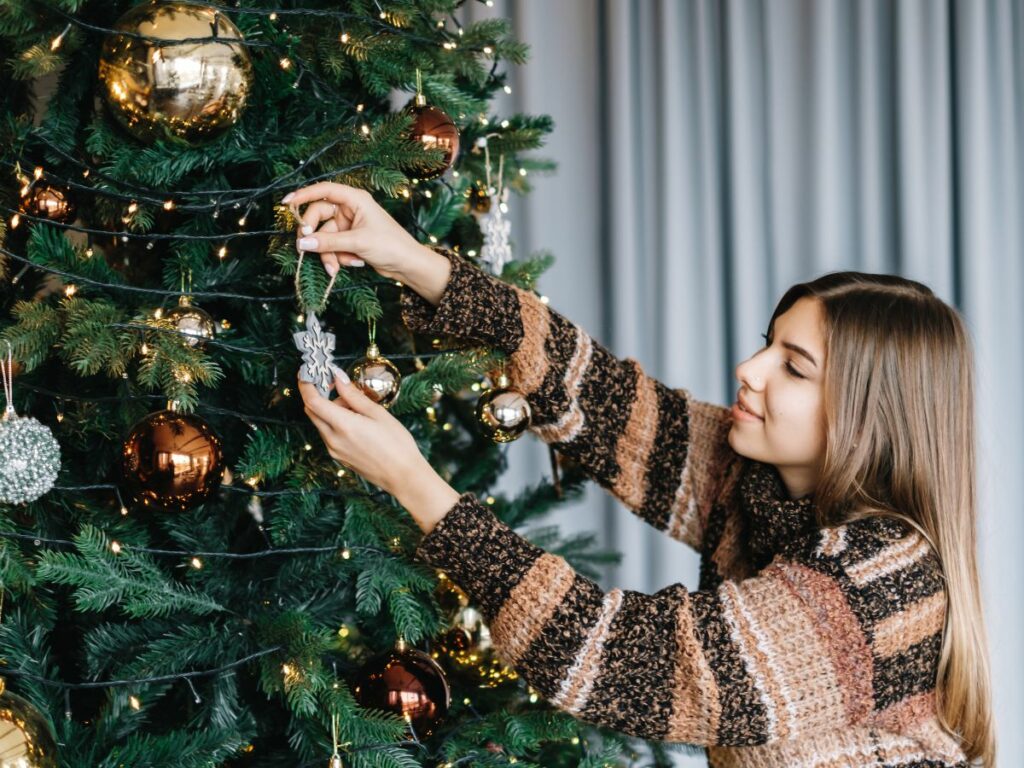 A woman decorates a christmas tree with ornaments.
