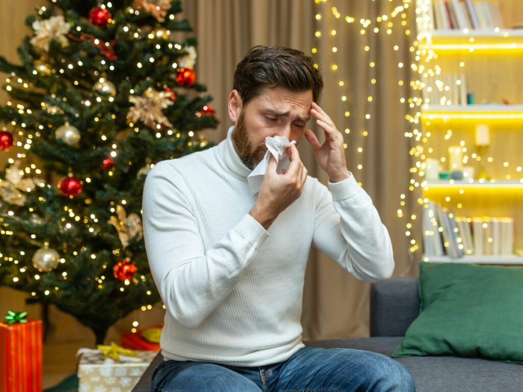 A man showing symptoms of allergies in a room with a Christmas tree.