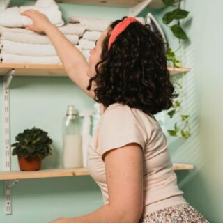 A woman is putting towels on a shelf in a laundry room.