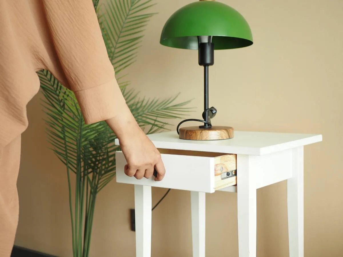 A woman organizing a drawer on a white nightstand.