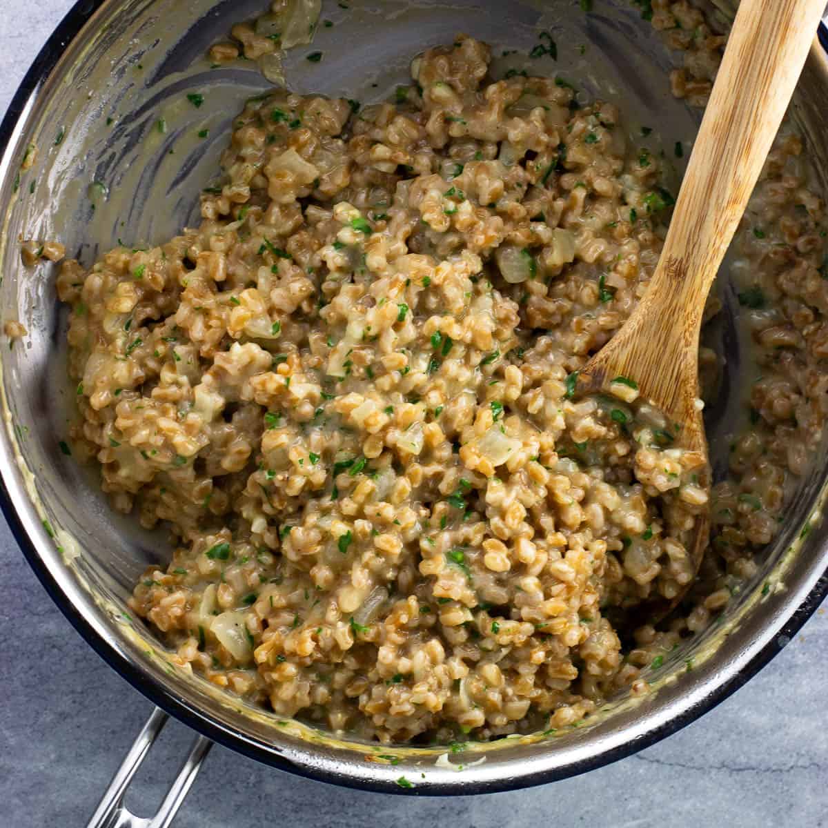 A bowl of farroto in a pan with a wooden spoon.