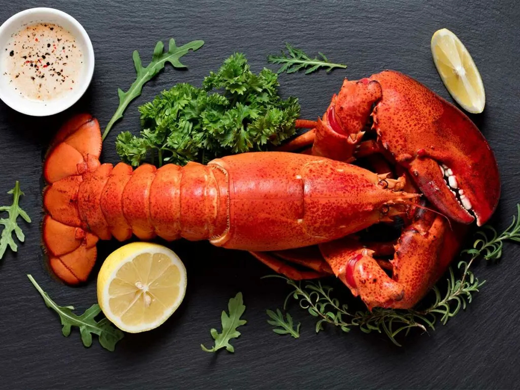 A lobster on a black table with lemons and herbs.