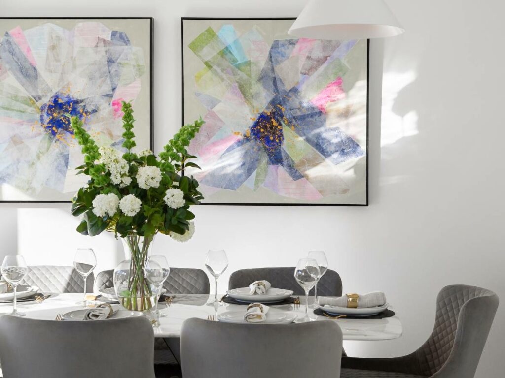 A dining room with two paintings on the wall and a set table.