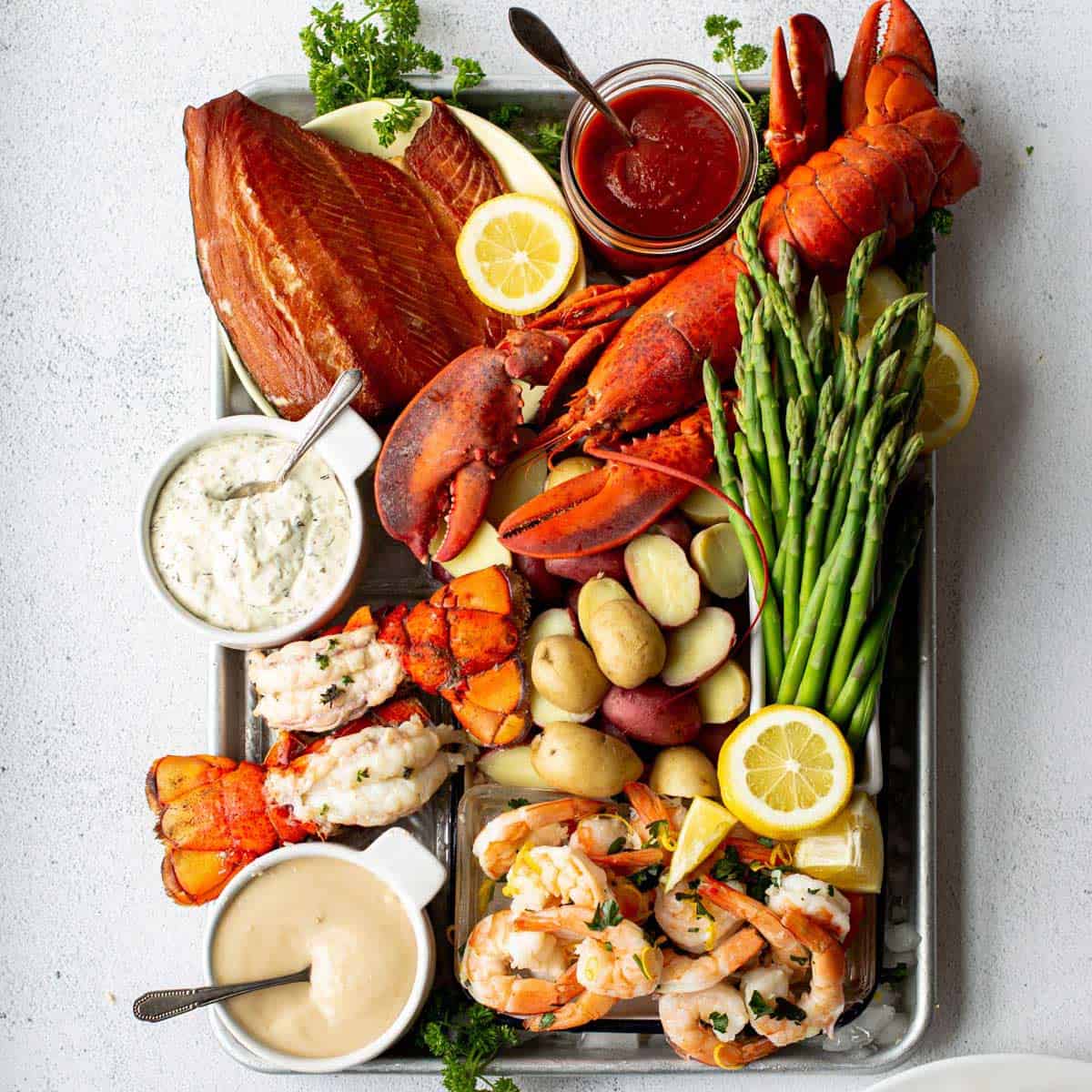 A tray of lobster, shrimp, and vegetables with three different kinds of sauce on a table.