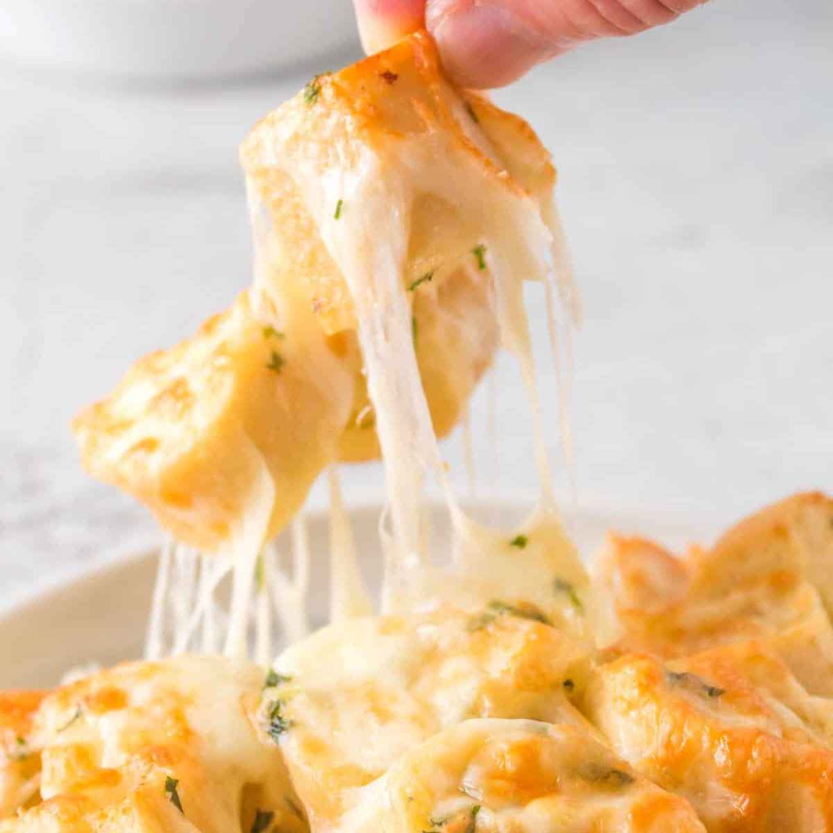 Person picking up cheesy bread from a white bowl.