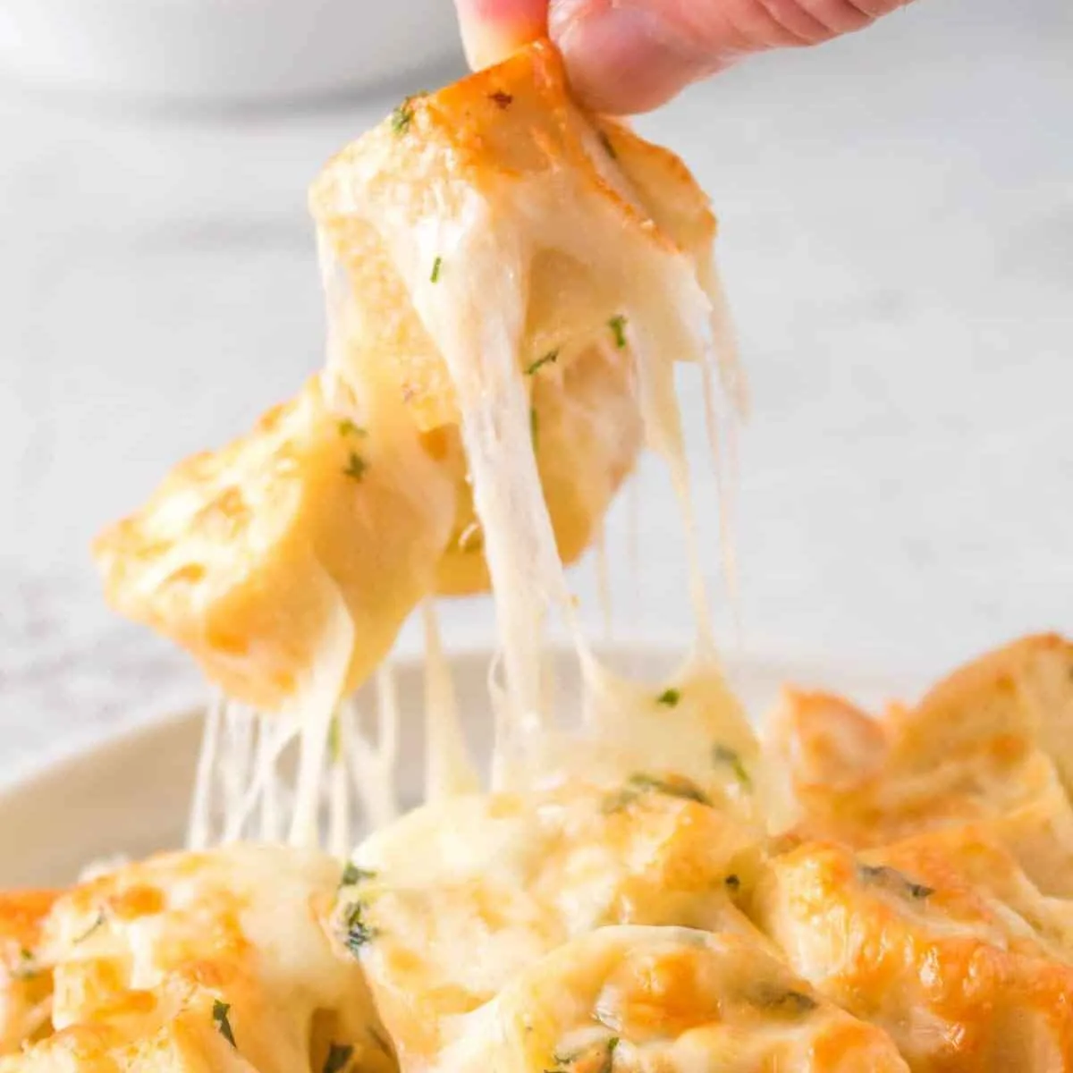 Person picking up cheesy bread from a white bowl.