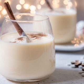 Two glasses of eggnog with cinnamon in them.