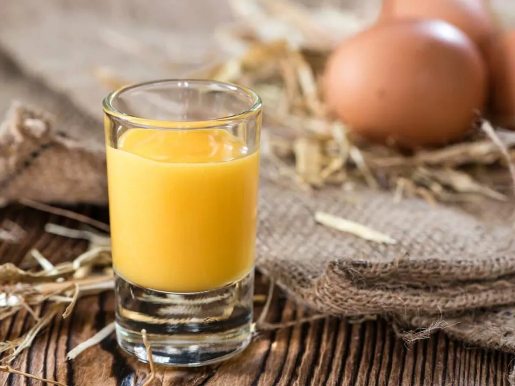 A glass of boiled custard next to some eggs.
