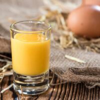 A glass of boiled custard next to some eggs.