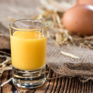 A glass of boiled custard next to some eggs.