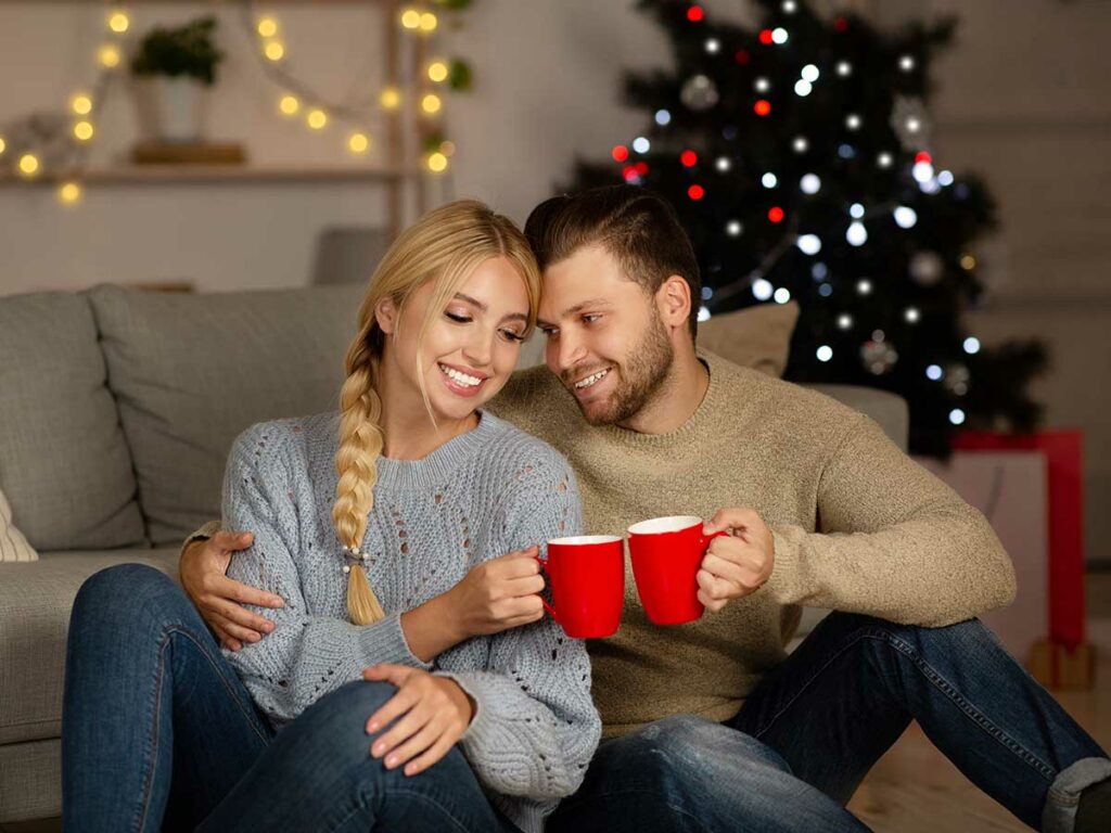 A man and woman sitting on the couch holding mugs of Christmas blend coffee.