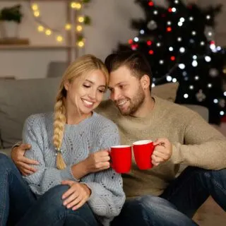 A man and woman sitting on the couch holding mugs of Christmas blend coffee.