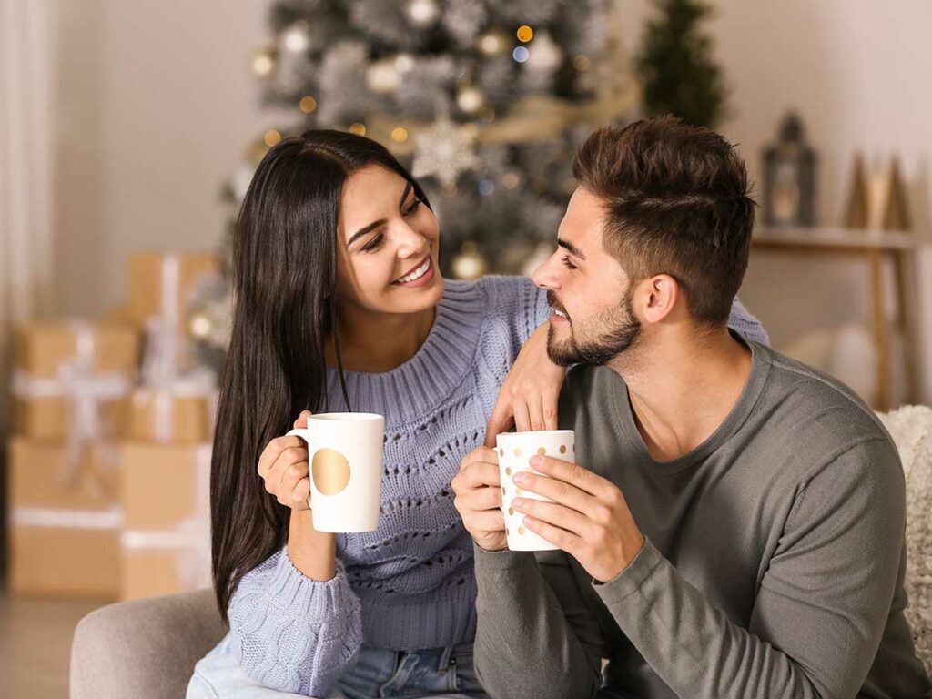 A man and woman sitting on a couch holding Christmas blend coffee mugs.