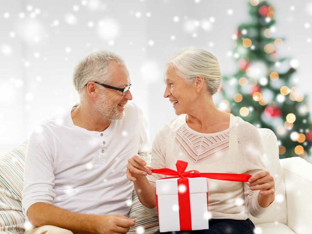 A senior woman opening a gift box in front of a Christmas tree.