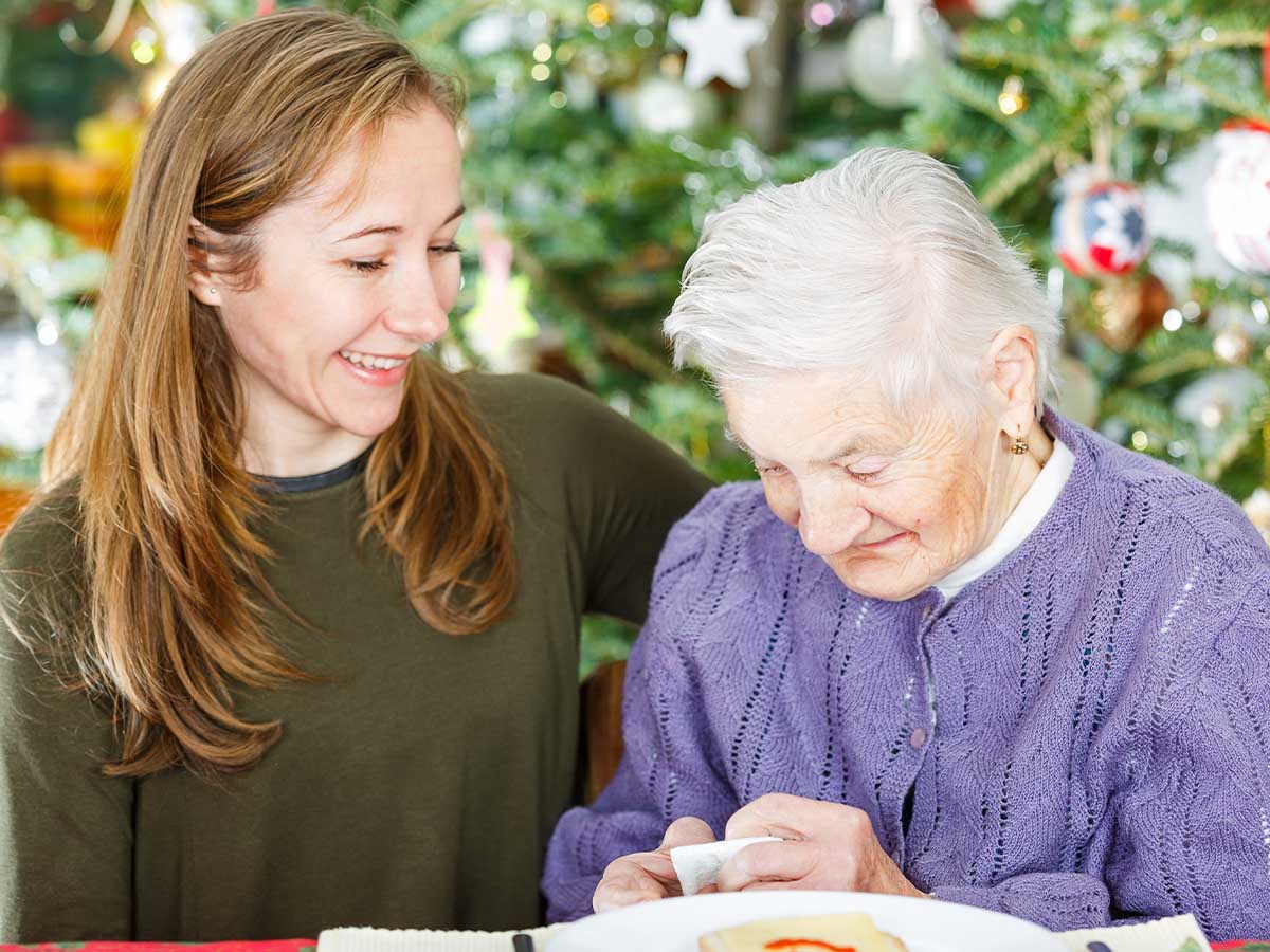 A young woman giving an elderly senior woman a Christmas gift.