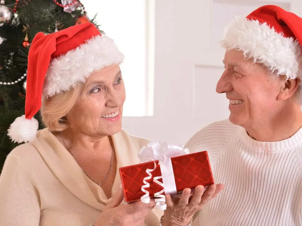 A couple in santa hats holding a Christmas present, perfect for older women.