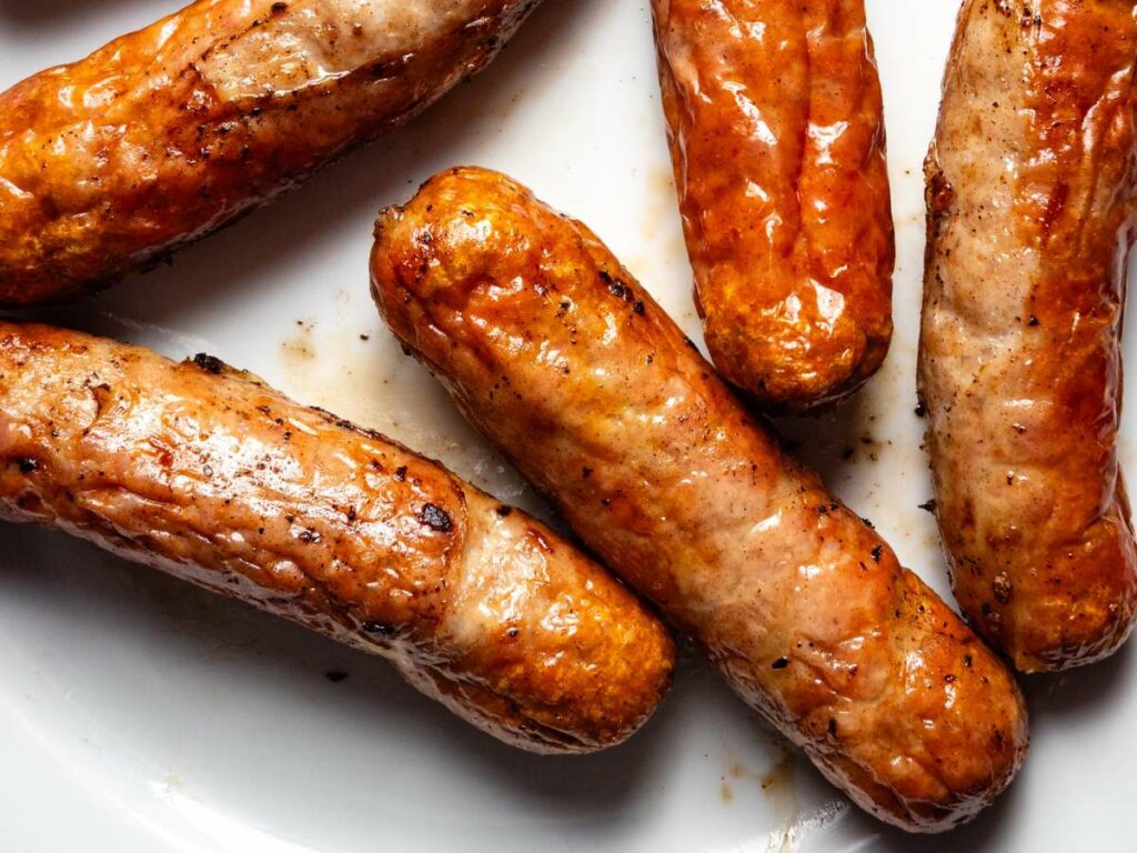 Cooked breakfast sausages on a plate on a white plate.