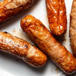 Cooked breakfast sausages on a plate on a white plate.