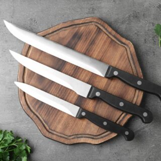 Three knives on a wooden cutting board with parsley.