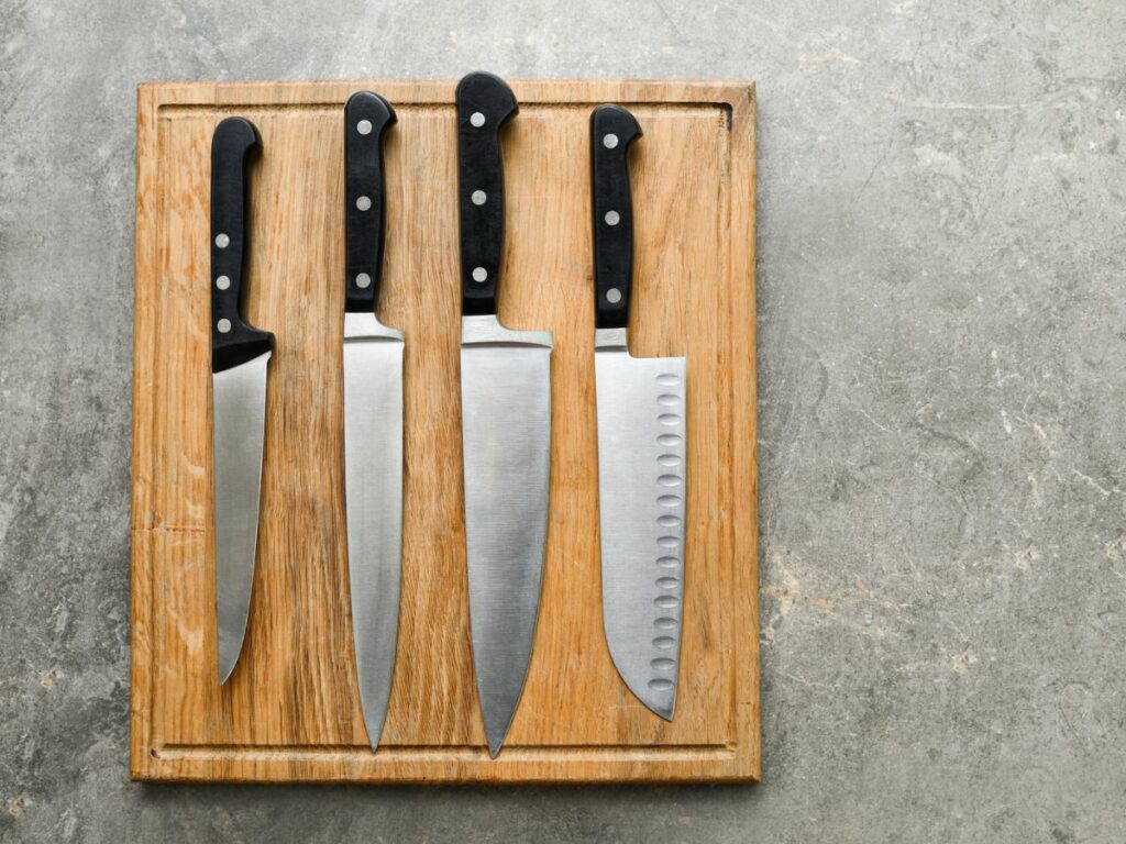 Four knives on a wooden cutting board.