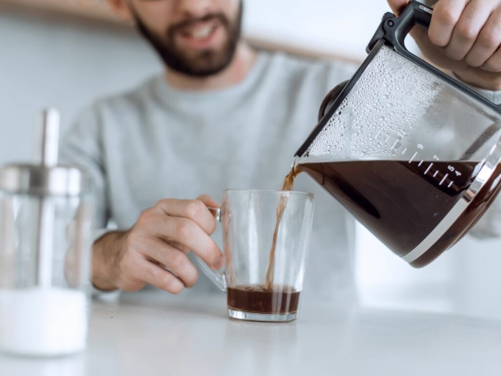 A man pouring coffee from a carafe into a glass.