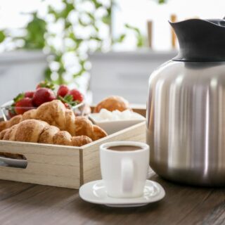 A stainless steel coffee carafe on a tray with croissants and a cup of coffee.